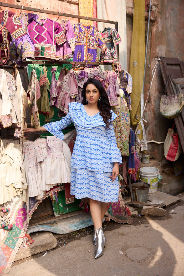 Woman in a blue dress standing in front of a colorful market stall.